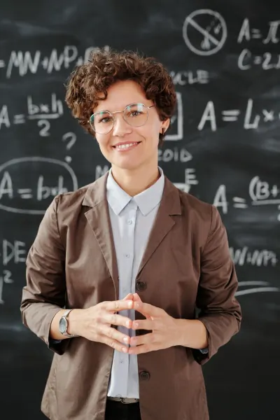 A woman teacher smiling in front of a chalkboard covered in equations